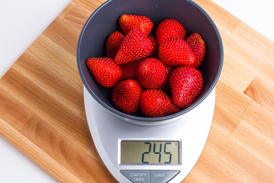 Wash and cut the tops off your strawberries 245 grams of strawberries in a blue bowl on a scale